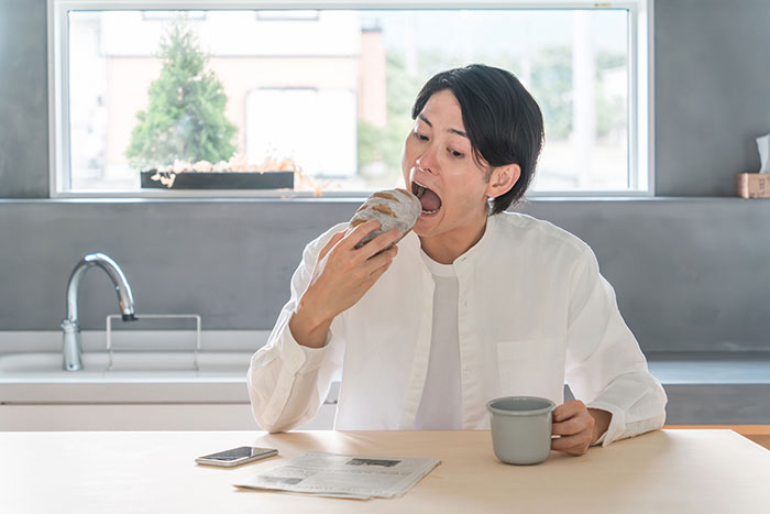 食卓で大口を開けてパンを頬張る男性